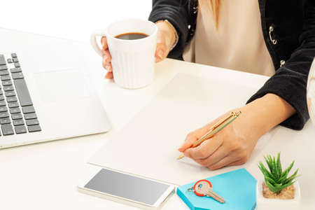 A businesswoman on her office is writing a note while holding a cup of coffee in her handの写真素材