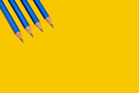 Four blue pencils in a corner of a yellow backgroundの写真素材