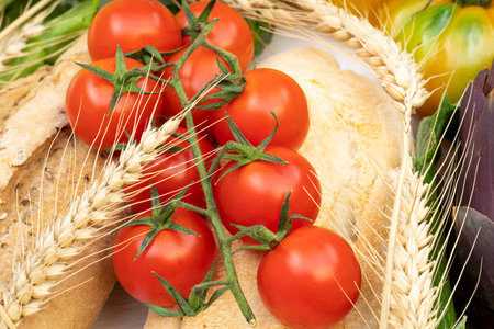 Close up of a bunch of cherry tomatoes with bread and ears of wheatの写真素材