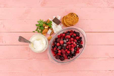 Berries with yogurt and cookies on a pink wooden tableの写真素材
