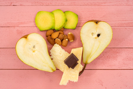 Pears and cheese with almonds and chocolate on a pink wooden tableの写真素材