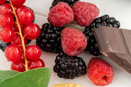 Close up of raspberries with blackberries, chocolate and currants on a white wooden tableの写真素材