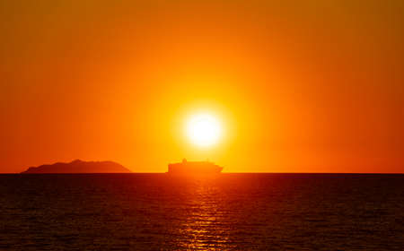 A backlit passenger ship near an island at sunsetの写真素材