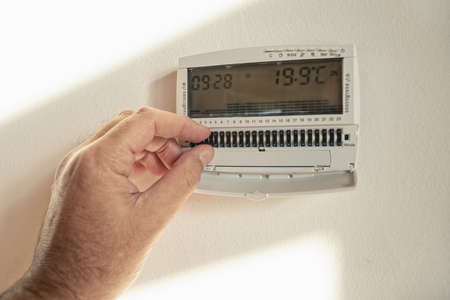 Male fingers setting temperature of thermostat in living roomの写真素材