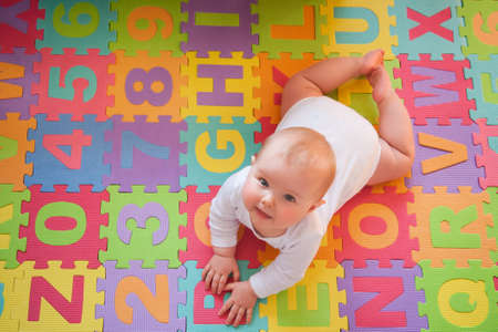 Cute baby looking up from colorful alphabet mat while playing on tummy.の写真素材
