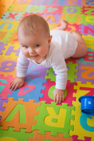 Happy blue-eyed baby learning to crawl on colorful alphabet mat.の写真素材