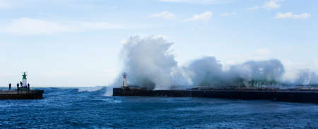 Waves crashing over lighthouse in Kalk Bay Harbour as fishermen brave storm, Cape Town, South Africa.の写真素材