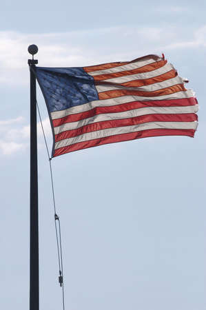 American flag with torn edges on flagpole blowing in the wind.