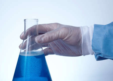 Hand on erlenmeyer flask filled with blue liquid blue tint with copyspace