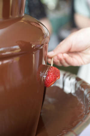 Chocolate fondue fountain with strawberry being dippedの写真素材