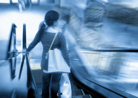 Blue motion blur of young woman with shopping bags on escalatorの写真素材