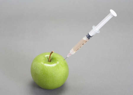 Syringe needle injected into green apple on greyの写真素材