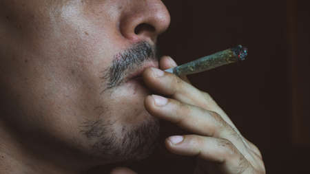 Caucasian man with facial hair smoking marijuana tobacco puffing smoke from mouth to nose
