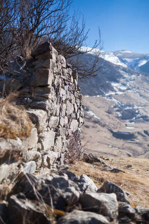 Stone wall in the mountains near the village of Dargavs. North Ossetia - Alania, Russia. With background of mountains and blue sky. Selective focus.の写真素材
