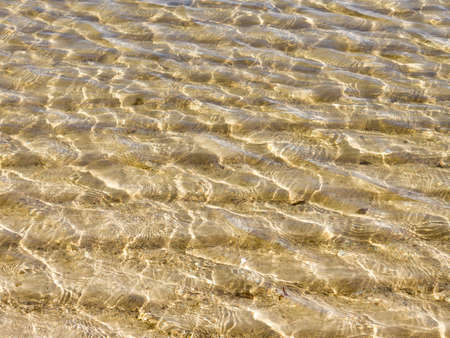 Sunlight plays in a transparent sea water and yellow sand