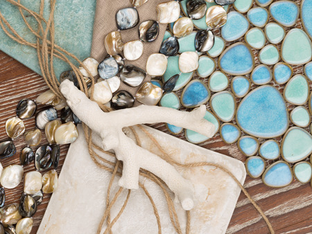 selection of materials in a nautical theme with a blue ceramic mosaic-like sea pebbles, antique ceramic tiles, a linen cloth, pearl beads, salted wood, twine and coralの写真素材