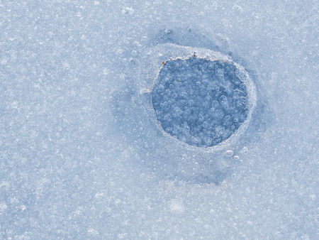 hole in the fragile surface of melting ice on the lake in the spring
