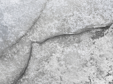 dangerous subtle but deep cracks in the gray soaked fragile ice on a lake in early springの写真素材