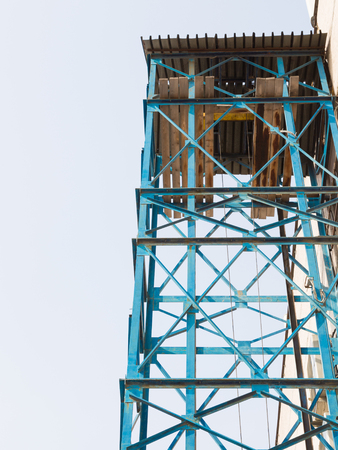 construction hoist with blue metal frame and wooden roof of boards for lifting loads to a height against the skyの写真素材