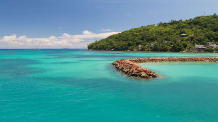 Lovely bright horizontal seascape with a breakwater made of stones in a clean transparent blue sea, Seychellesの写真素材
