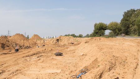 construction of a new road with light yellow sand fines on the construction site and the old road with an arch of trees goes closeの写真素材