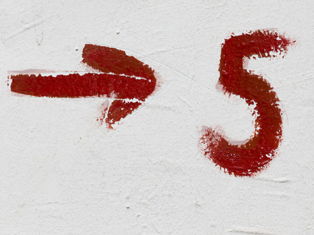 bright red number five and arrow drawn on rough paint old painted wallの写真素材