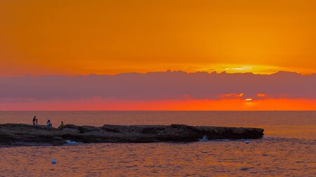 El Campello - October 3, 2015: People watch the sunrise and take photos at the edge of a stone cliff in the early morning, and the sea around October 3, 2015, El Campello, Costa Blanca, Spainのeditorial素材