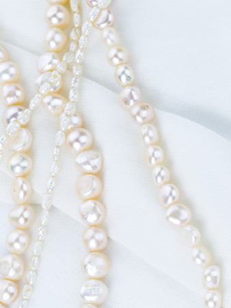 beautiful white beads made from freshwater pearls with a matte sheen on white fabric with folds...