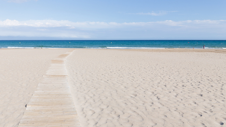 Light wooden walkway through the city sandy beach leads to the blue seaの写真素材