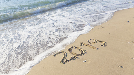 Figures of the new year 2019 are written on the clean yellow sand on the beach and the sea waves with foam roll ashoreの写真素材