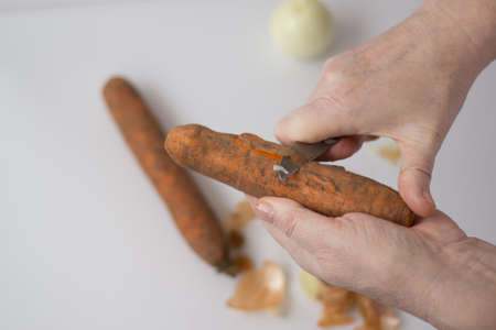 hands of an elderly woman peel vegetables carrots and onions with a knifeの写真素材