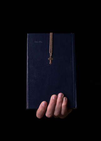 Bible with a cross in his hand on a black backgroundの写真素材