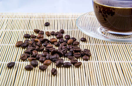 A cup of coffee with scattered grains on a bamboo napkinの写真素材