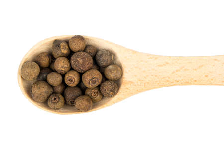 Dry grains allspice in a wooden spoon on a white background