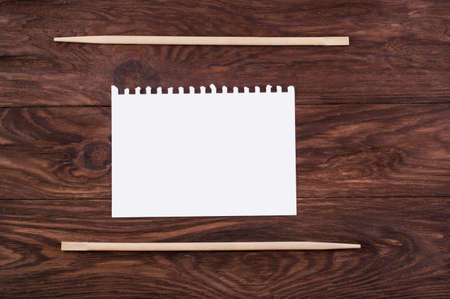 Chopsticks and a blank sheet of paper for recipes and menus on a wooden brown backgroundの写真素材