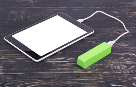 Tablet PC charged by the mobile charger on a wooden dark backgroundの写真素材