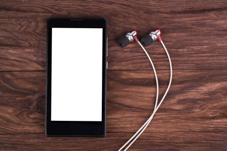Mobile phone with white headphones on a brown wooden backgroundの写真素材