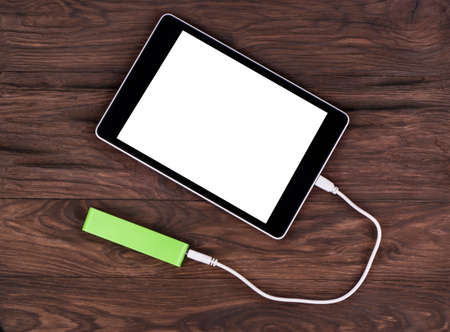 Tablet PC charged by the mobile charger on a wooden brown backgroundの写真素材