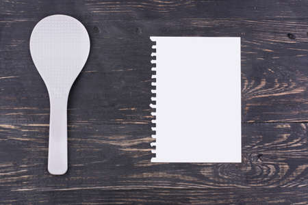 White plastic spoon and a blank sheet of paper for writing recipes and menus on a wooden backgroundの写真素材