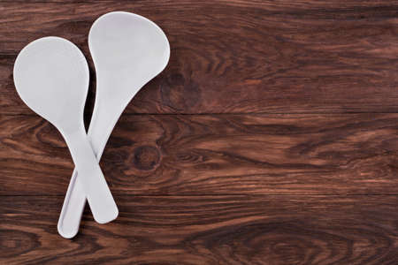 White plastic kitchen ladle and spoon on a brown wooden backgroundの写真素材