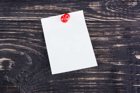Blank sticker attached red pushpin on a dark wooden board