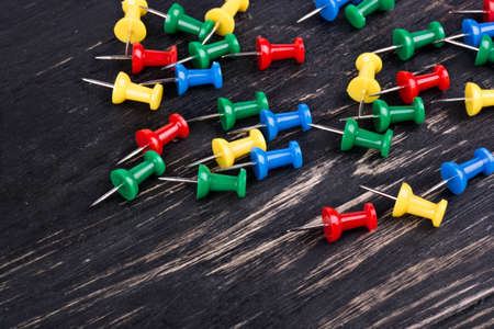 The scattered multicolored pushpins on dark wooden background