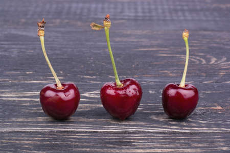 Three fresh red cherries on a dark wooden backgroundの写真素材