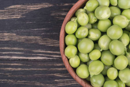 Fresh green peas in a wooden bowl on a wooden background top viewの写真素材