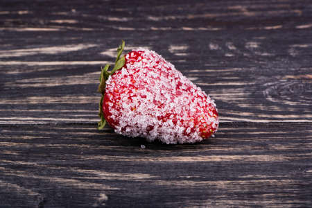 Ripe red strawberries covered in sugar crystals on a dark wooden backgroundの写真素材
