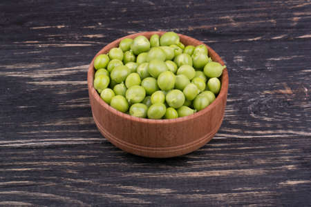 Fresh green peas in a wooden bowl on dark wooden backgroundの写真素材