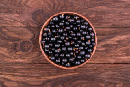 Bowl full of fresh black currant on a wooden background top viewの写真素材