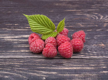 Fresh raspberries with leaves on a dark wooden background