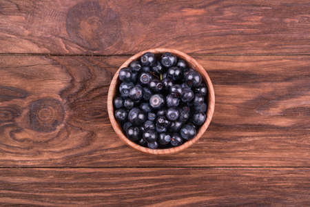 Bowl full of fresh blueberries on a wooden background top view