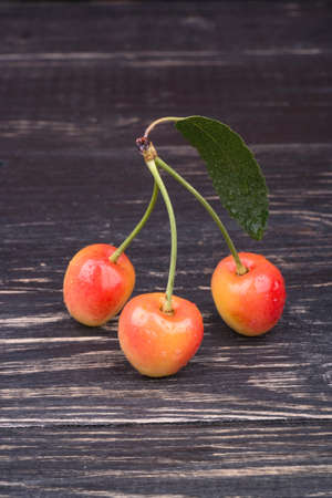 Three fresh yellow cherry with a leaf on a dark wooden background